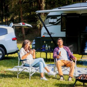 Couple relaxing at campsite beside caravan with drinks