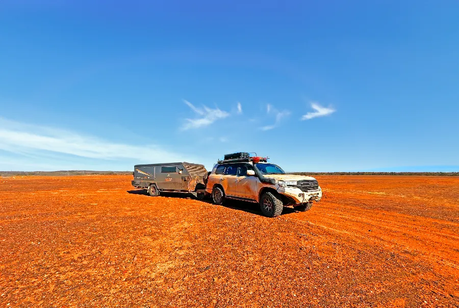 SUV and trailer on a vast, red dirt plain.