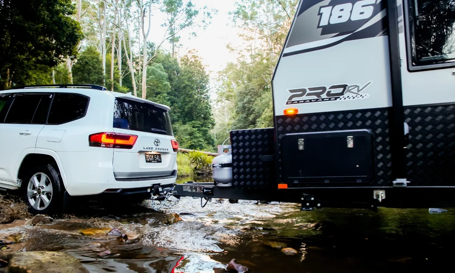 SUV towing a caravan through a rocky creek